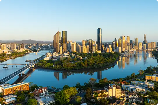 Aerial view of a city skyline with tall buildings, bridges, and a winding river surrounded by greenery under a clear blue sky during daylight.